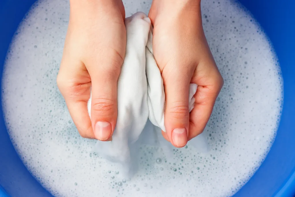 a close up of someone cleaning made-to-measure curtains by hand in a blue bucket