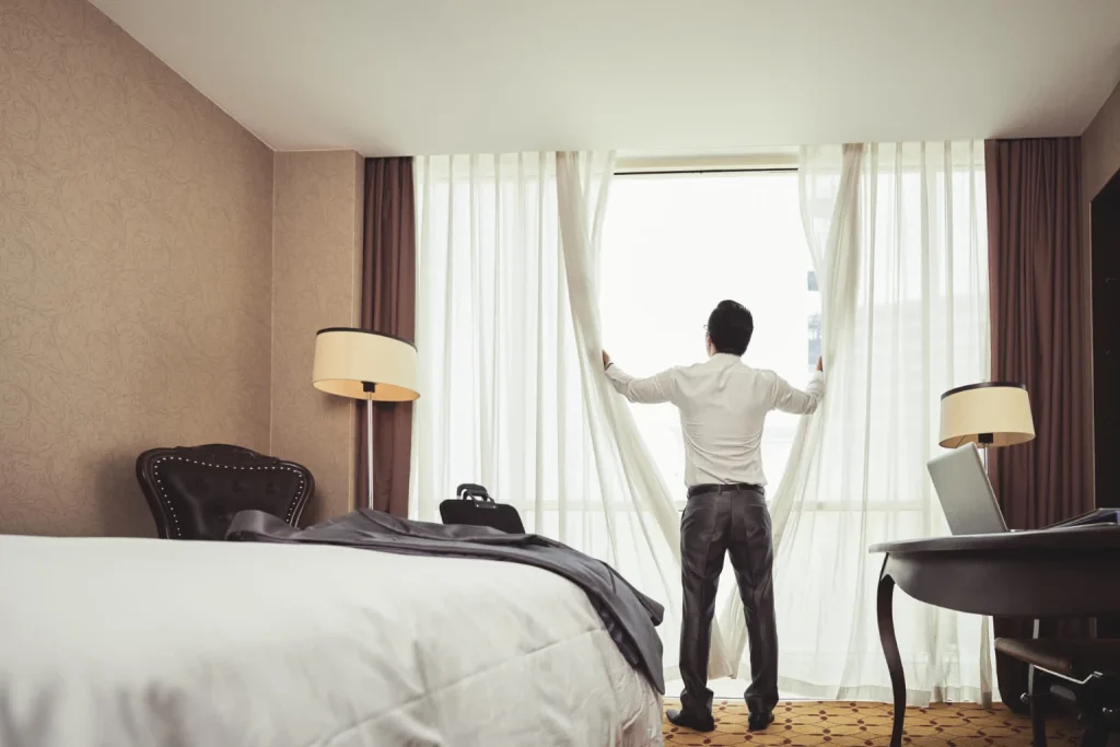A man shutting made-to-measure curtains in a hotel room